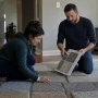 A couple is comparing carpet samples on a living room floor in natural lighting